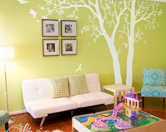May include: A white tree wall decal with birds, a white couch with green pillows, a wooden table with a toy playset, and a green wall.