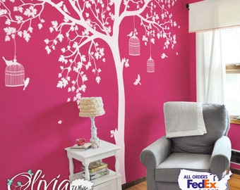 May include: A large white wall decal featuring a sprawling tree with intricate leaves, branches, and hanging birdcages. Several small birds are positioned on the branches and near the cages. The decal is applied to a vibrant, solid hot pink wall.