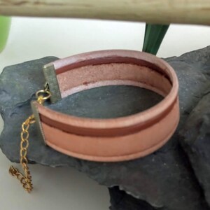 May include: A light brown leather bracelet with a gold chain and clasp. The bracelet has a brown and white striped design.