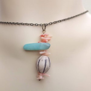 Peut inclure: Un collier d&eacute;licat avec un pendentif compos&eacute; d'une pierre bleu clair, d'une perle &agrave; motif blanc et noir et de morceaux de corail rose.