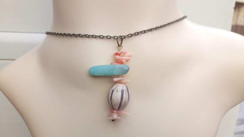 Peut inclure: Un collier d&eacute;licat avec un pendentif compos&eacute; d'une pierre bleu clair, d'une perle &agrave; motif blanc et noir et de morceaux de corail rose.