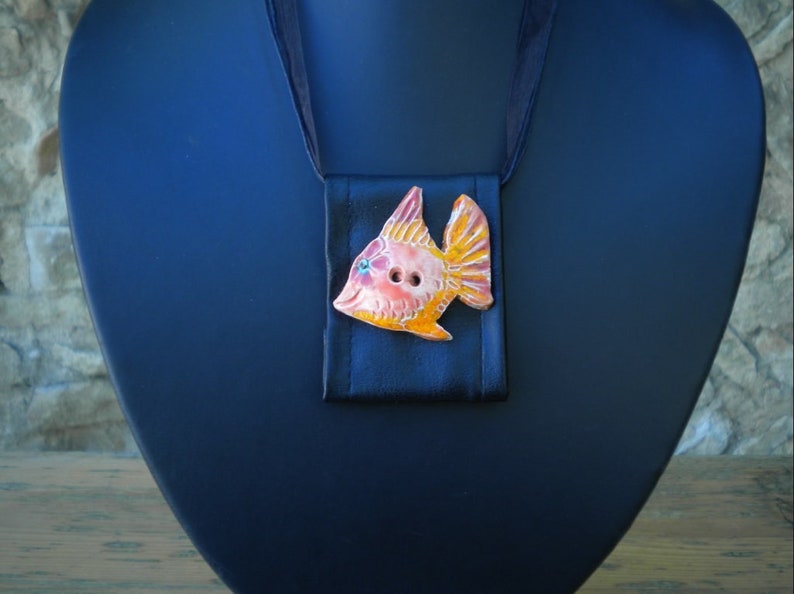 Pu&ograve; includere: Una collana con un ciondolo a forma di pesce in ceramica, smaltato in arancione, rosa e giallo. Il pesce ha due bottoni neri per gli occhi ed &egrave; attaccato a un nastro di raso nero.