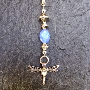 Puede incluir: Un collar de plata con un colgante de piedra azul y un dije de lib&eacute;lula.
