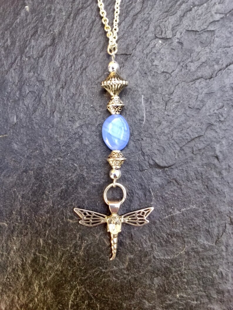Puede incluir: Un collar de plata con un colgante de piedra azul y un dije de lib&eacute;lula.