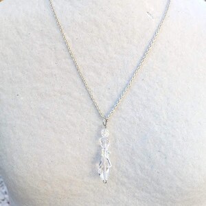 May include: A silver chain necklace with a clear crystal pendant. The pendant is shaped like a teardrop and has a faceted design.