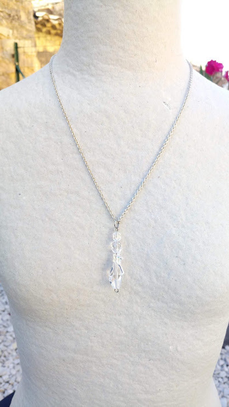 May include: A silver chain necklace with a clear crystal pendant. The pendant is shaped like a teardrop and has a faceted design.