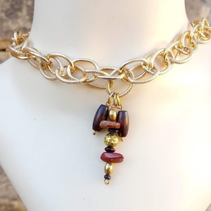 Könnte beinhalten: Eine goldene Ketten-Choker-Halskette mit einem Anhänger aus braunen und roten Holzperlen und goldenen Akzenten.