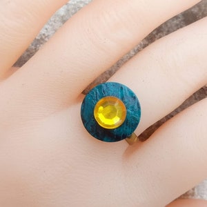 Peut inclure: Une bague bleu turquoise avec un strass jaune au centre.