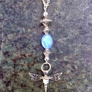 Puede incluir: Un collar de cadena de plata con una cuenta de vidrio azul, un dije de lib&eacute;lula de plata y un colgante de plata con detalles intrincados.