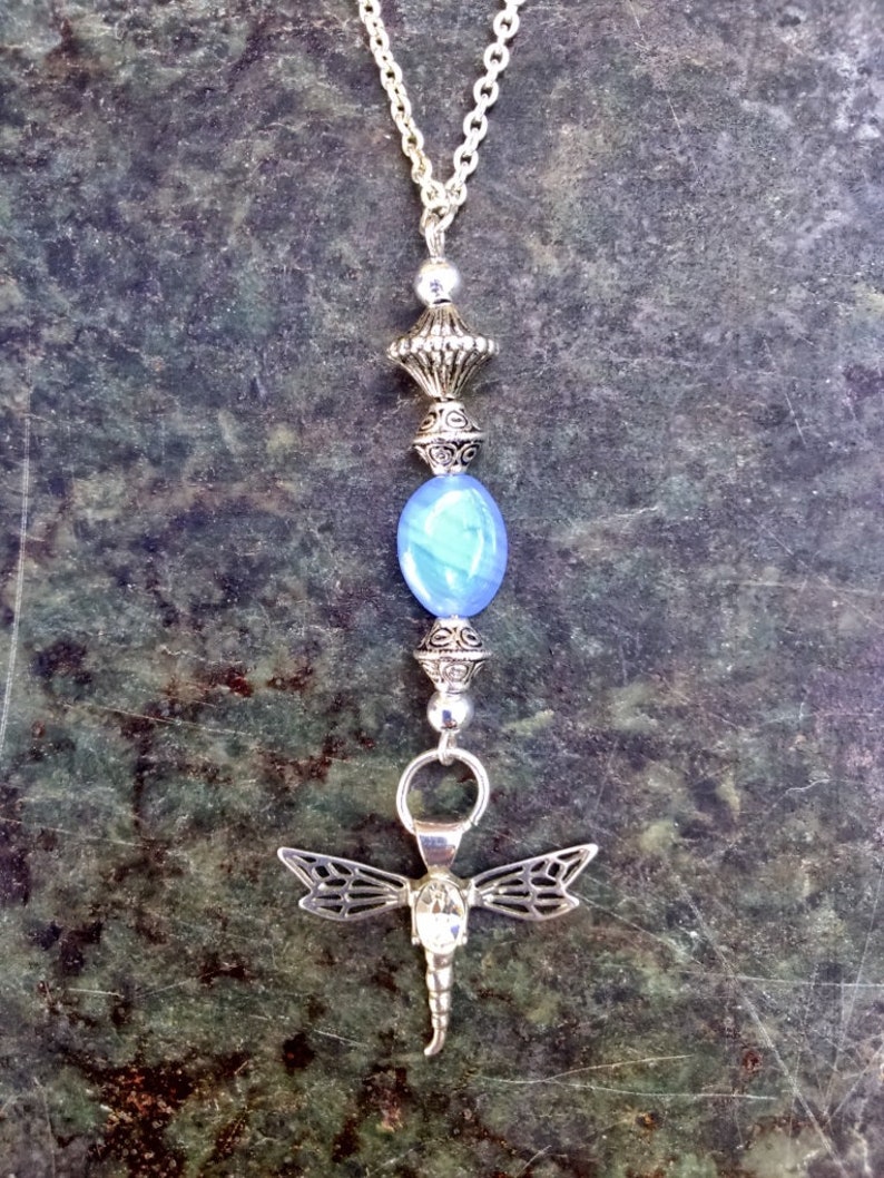 Puede incluir: Un collar de cadena de plata con una cuenta de vidrio azul, un dije de lib&eacute;lula de plata y un colgante de plata con detalles intrincados.