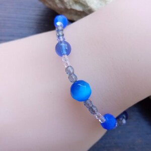Puede incluir: Un brazalete de cuentas azules y grises con una banda el&aacute;stica extensible. El brazalete presenta cuentas redondas azules con un acabado brillante y cuentas m&aacute;s peque&ntilde;as grises y transparentes.