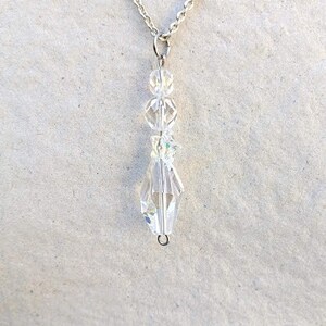 May include: A silver chain necklace with a crystal pendant. The pendant is made of several clear crystal beads and has a teardrop shape.