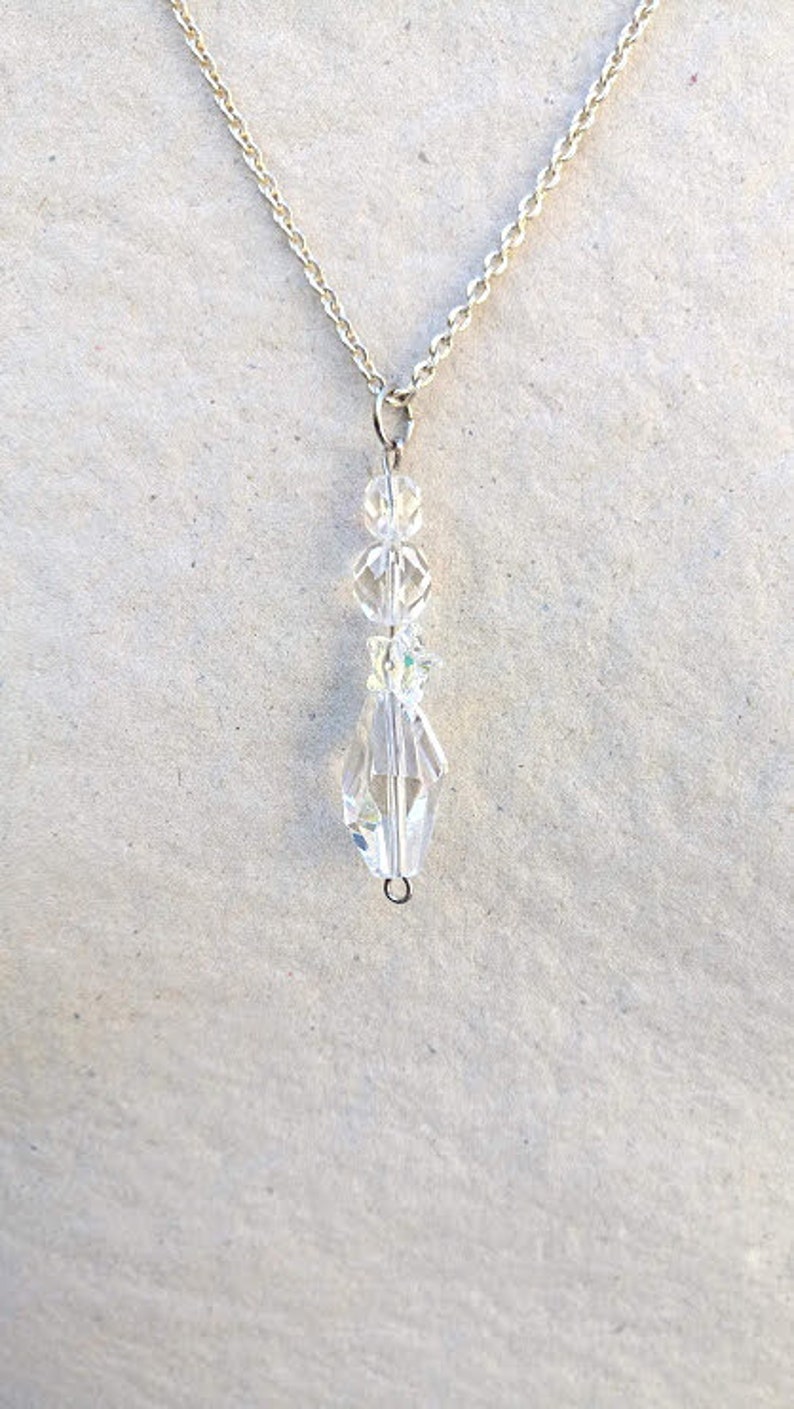 May include: A silver chain necklace with a crystal pendant. The pendant is made of several clear crystal beads and has a teardrop shape.