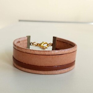 May include: A light brown leather bracelet with a brown leather band and a gold clasp.