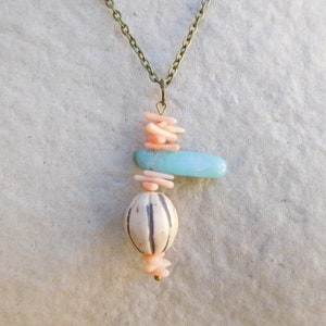 Peut inclure: Un collier avec un pendentif compos&eacute; d'une pierre bleu clair, d'une perle &agrave; motif blanc et noir et de perles de corail rose. Le collier est fait d'une cha&icirc;ne en laiton.