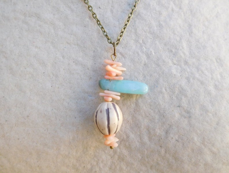 Peut inclure: Un collier avec un pendentif compos&eacute; d'une pierre bleu clair, d'une perle &agrave; motif blanc et noir et de perles de corail rose. Le collier est fait d'une cha&icirc;ne en laiton.