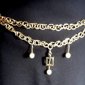 Peut inclure: Une ceinture en chaîne dorée avec trois perles pendantes et un pendentif carré. La ceinture est superposée et présente un design de chaîne épaisse.