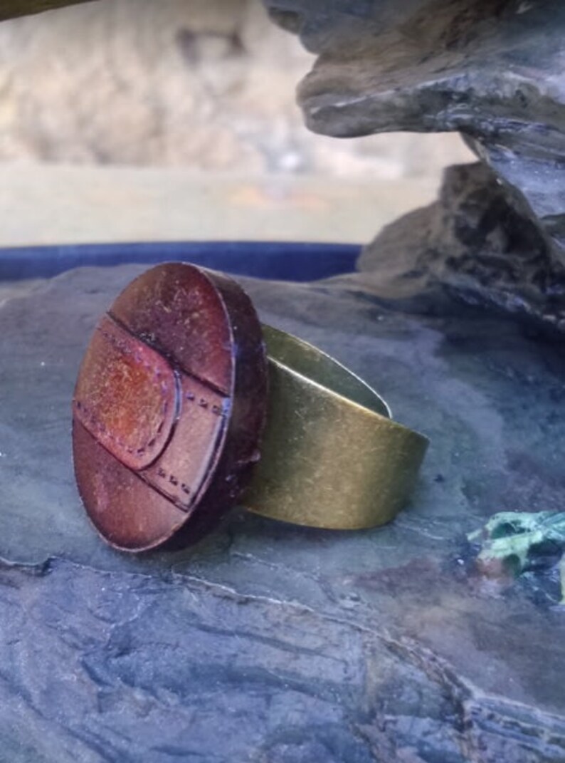 Op de afbeelding: Een ring met een grote, ovale, bruine hars steen met een gouden band. De steen heeft een getextureerd oppervlak met een patroon van lijnen en cirkels.