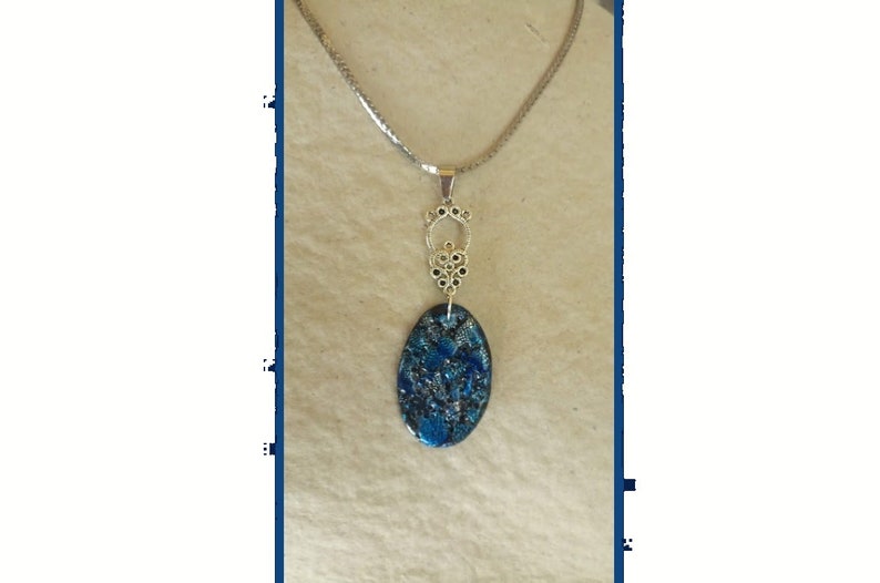 May include: A silver-toned necklace with an oval pendant. The pendant features a blue and black speckled design. The necklace has a decorative silver bail and a delicate chain.