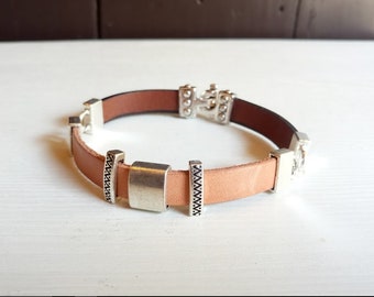 May include: A brown leather bracelet with silver metal accents. The bracelet has a clasp closure and decorative metal pieces.