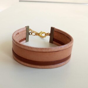 May include: A light brown leather bracelet with a brown stripe and a gold clasp.