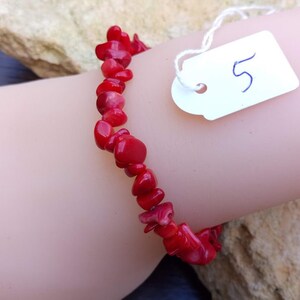 May include: Red coral chip bracelet. The bracelet is on a mannequin wrist. A white tag with the number 5 is attached to the bracelet.