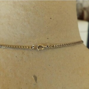 May include: A silver-toned necklace with a snake chain design. The necklace is fastened with a lobster clasp. The necklace is displayed on a mannequin.