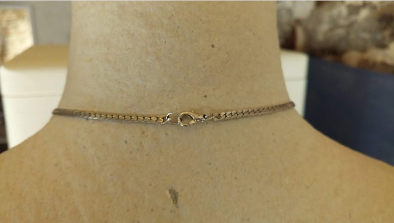 May include: A silver-toned necklace with a snake chain design. The necklace is fastened with a lobster clasp. The necklace is displayed on a mannequin.