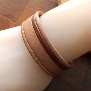 May include: A brown leather bracelet with a lighter brown leather strip running down the center.