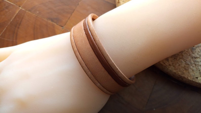 May include: A brown leather bracelet with a lighter brown leather strip running down the center.