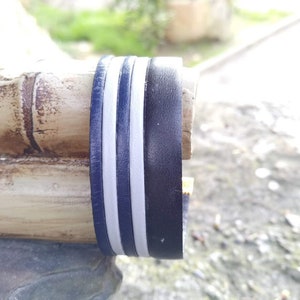 May include: Close-up of a wooden object with a black and white striped band around it. The band is made of two white stripes and a black stripe.
