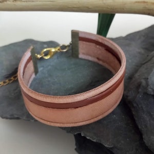 May include: A light brown leather bracelet with a brown leather strip and a gold clasp.