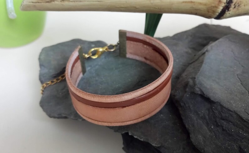 May include: A light brown leather bracelet with a brown leather strip and a gold clasp.