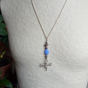 Puede incluir: Un collar de cadena de plata con una piedra ovalada azul y un colgante de lib&eacute;lula.