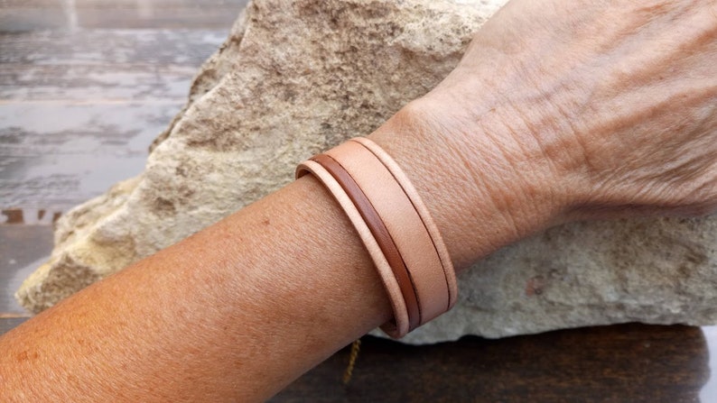 May include: A double-layered leather bracelet in shades of brown and beige. The bracelet is made of two strips of leather that are woven together.