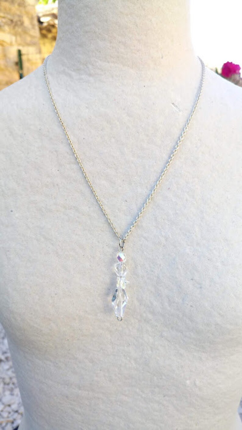 May include: A silver chain necklace with a clear crystal pendant. The pendant is made of faceted crystals that are arranged in a teardrop shape.