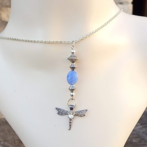 Puede incluir: Un collar de cadena de plata con un colgante de piedra azul y un dije de lib&eacute;lula.