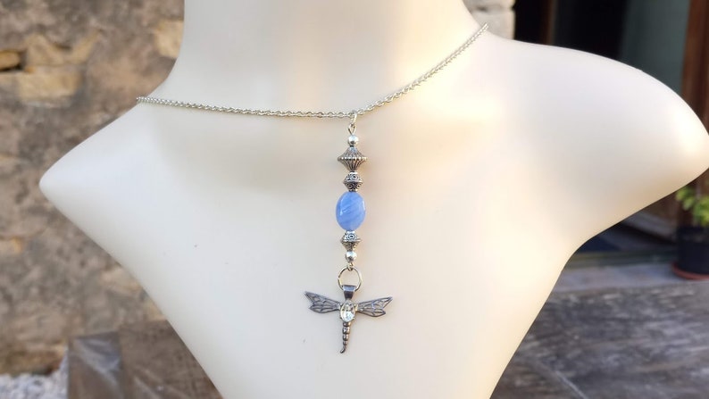 Puede incluir: Un collar de cadena de plata con un colgante de piedra azul y un dije de lib&eacute;lula.