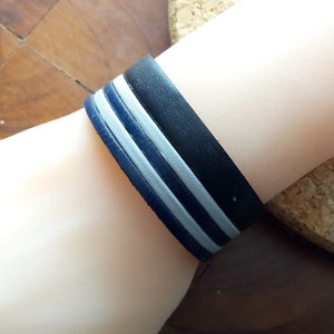 May include: A black leather bracelet with three white stripes.