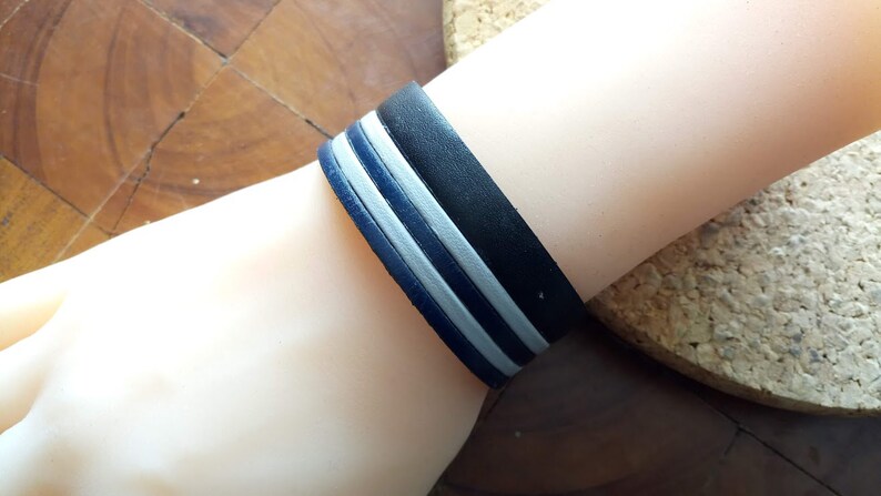 May include: A black leather bracelet with three white stripes.