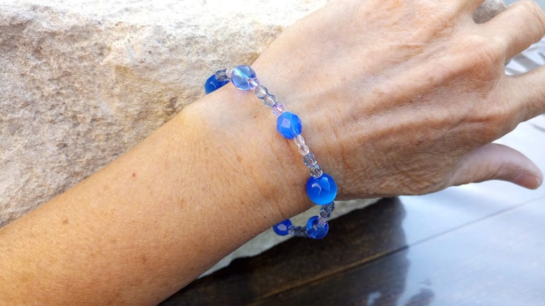 Puede incluir: Un brazalete de cuentas de vidrio azul y transparente con una banda el&aacute;stica.