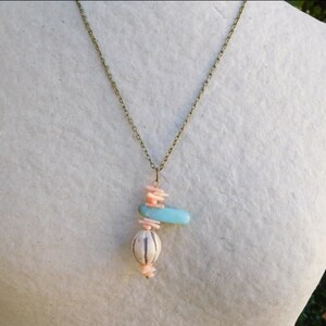 Peut inclure: Un collier avec un pendentif en turquoise, rose et blanc. Le pendentif est en forme de croix avec une perle ronde au bas.