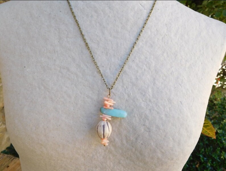Peut inclure: Un collier avec un pendentif en turquoise, rose et blanc. Le pendentif est en forme de croix avec une perle ronde au bas.