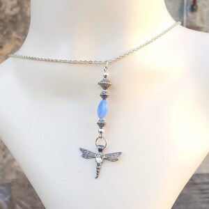 Puede incluir: Un collar de cadena de plata con una piedra preciosa azul y un colgante de lib&eacute;lula.