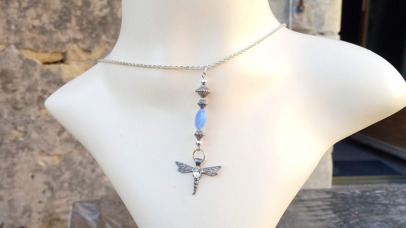 Puede incluir: Un collar de cadena de plata con una piedra preciosa azul y un colgante de lib&eacute;lula.