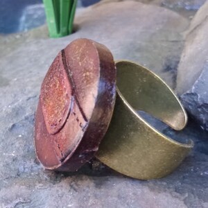 Op de afbeelding: Een verstelbare ring met een grote, ovale, bruine steen. De steen heeft een getextureerd oppervlak en een gouden ontwerp.