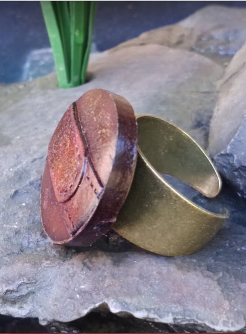 Op de afbeelding: Een verstelbare ring met een grote, ovale, bruine steen. De steen heeft een getextureerd oppervlak en een gouden ontwerp.
