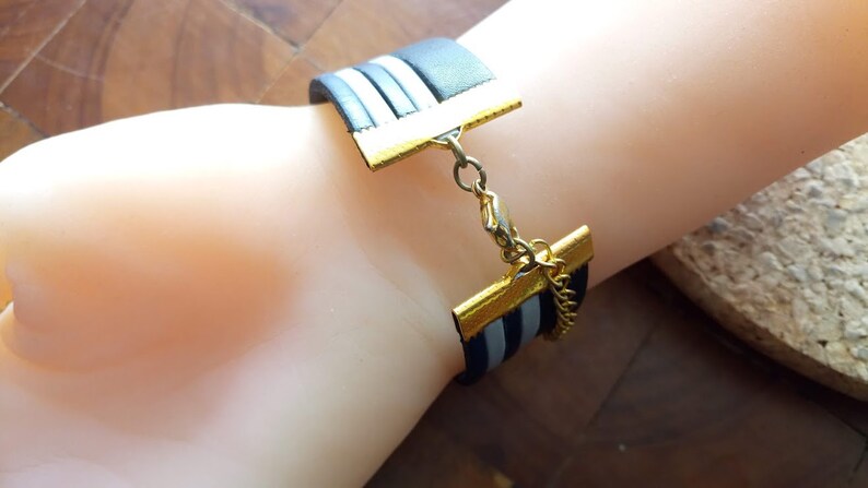 May include: A black and white striped leather bracelet with a gold clasp and chain. The bracelet is adjustable and has a simple design.