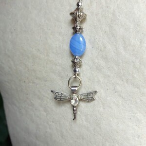 Puede incluir: Un collar de cadena de plata con una cuenta de &aacute;gata azul y un colgante de lib&eacute;lula de plata.