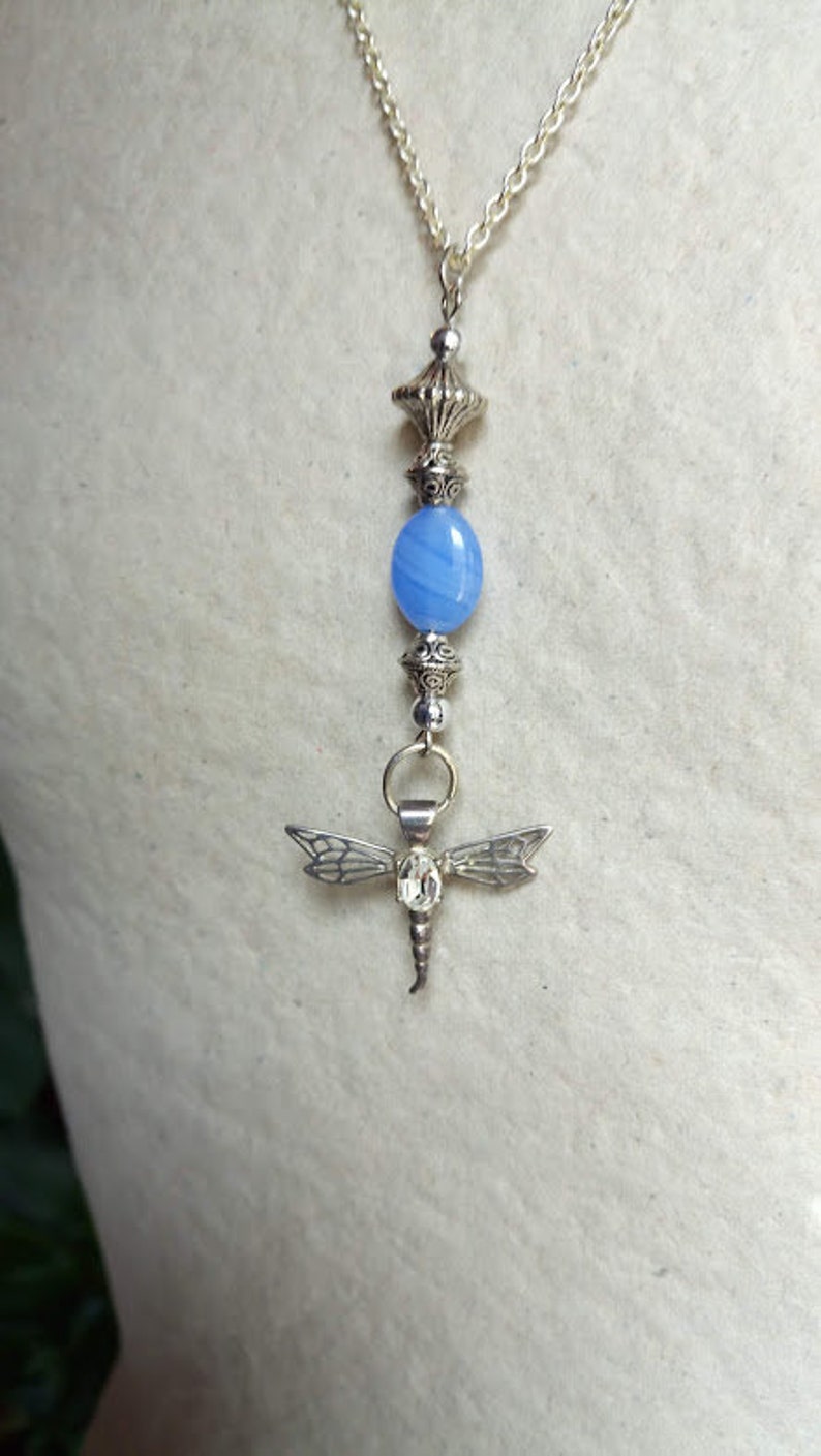 Puede incluir: Un collar de cadena de plata con una cuenta de &aacute;gata azul y un colgante de lib&eacute;lula de plata.